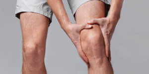 person in shorts holding left knee in pain