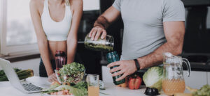 a couple at the kitchen bend with fruit and a juice jug pouring a glass of juice