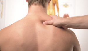 therapist squeezing the shoulder muscles of a patient sitting down