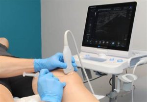 clinician injection a patients knee while holding an ultrasound probe