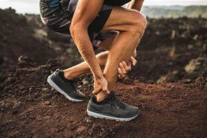 image: runner kneeling over and holding achilles