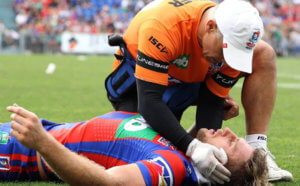 Image: rugby player laying on the groun unconscious being assessed by a medical staff member