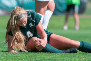 image: young female soccer player laying on ground holding her knee in pain