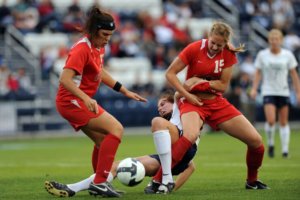 image fo 2 female soccer players tackling another female soccer player during a match