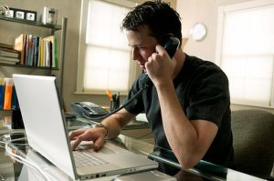 man sitting in home office on a laptop while talking on the phone